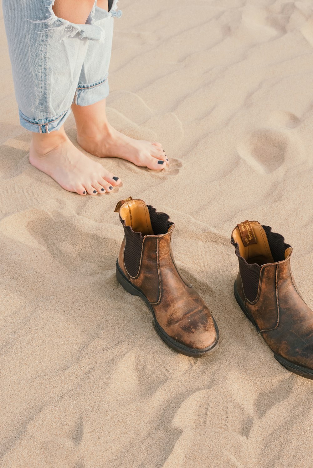 a pair of brown boots sitting on top of a sandy beach