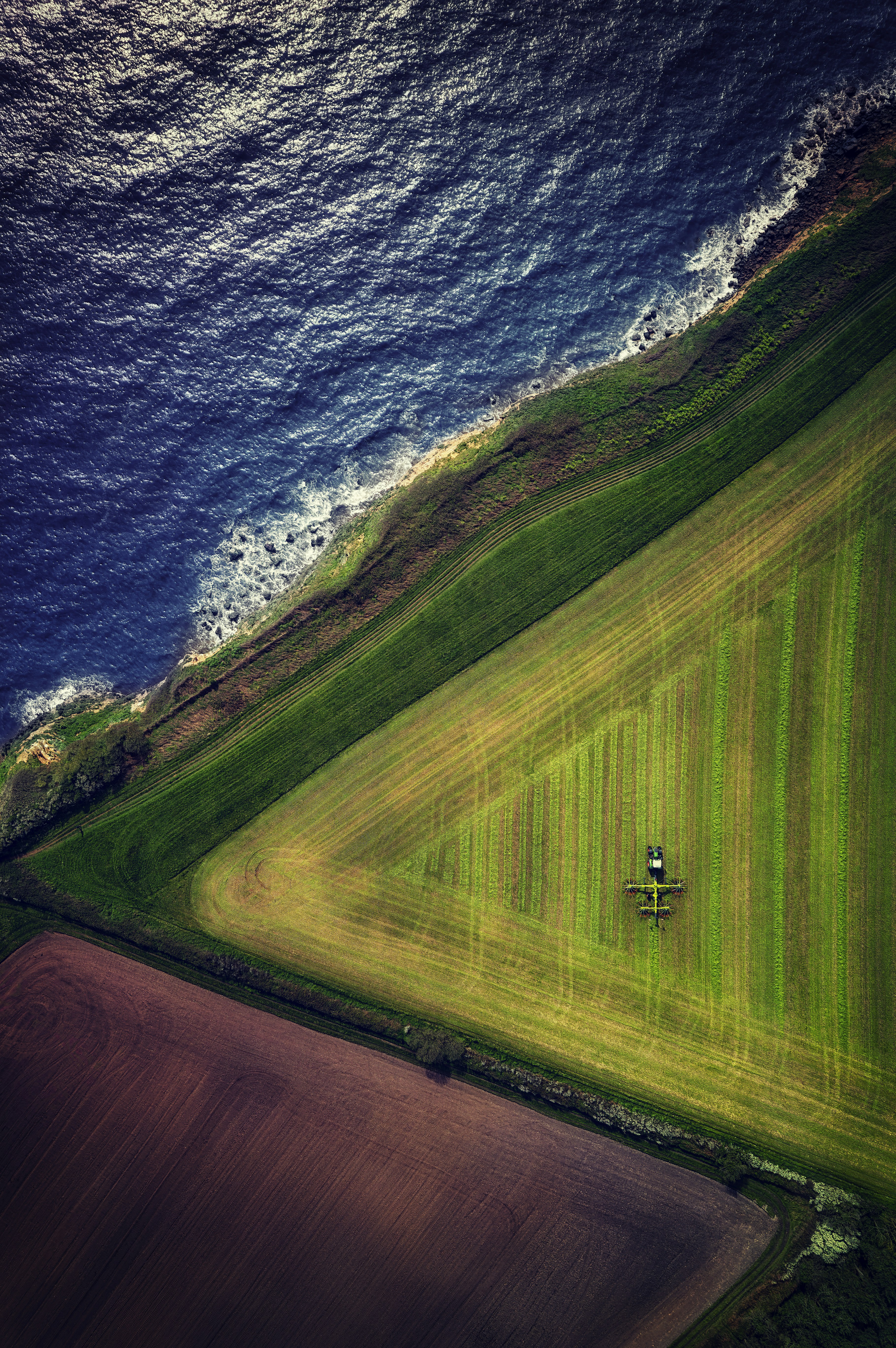 an aerial view of a green field next to the ocean