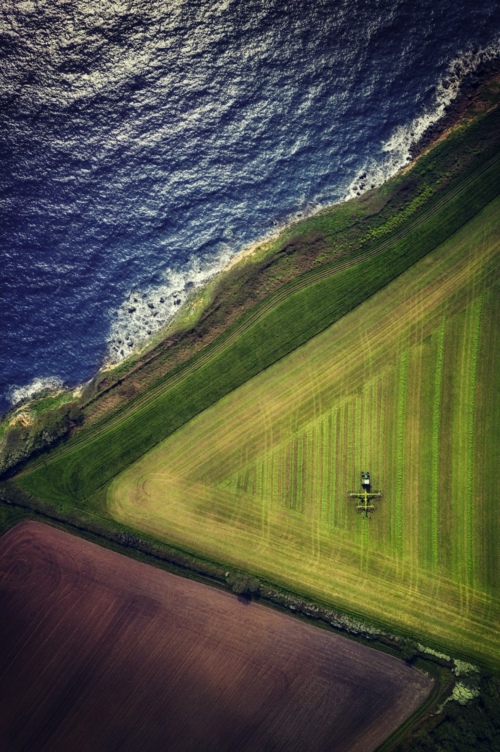 an aerial view of a green field next to the ocean