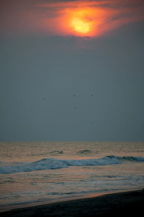 Sunset over a serene beach with gentle waves and vibrant orange skies.