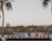 A colorful, artistic sign spells out 'Todos Santos' against a backdrop of lush palm trees. The sky is clear with a hint of a sunset, providing a calm and serene atmosphere.