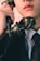 A close-up view of a person holding an old-fashioned rotary phone headset near their mouth, dressed in a formal suit and polka-dotted tie. The image captures the lower half of the face and emphasizes the vintage style of the telephone.