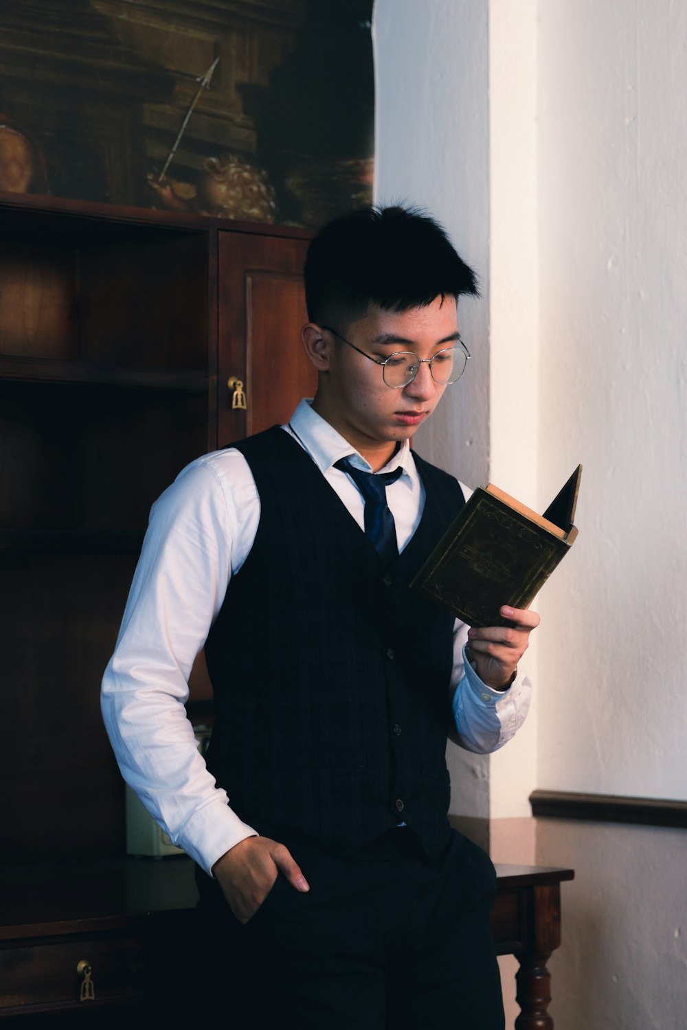 a man in a vest and tie reading a book