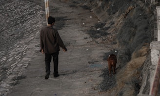 a man walking down a sidewalk next to a dog