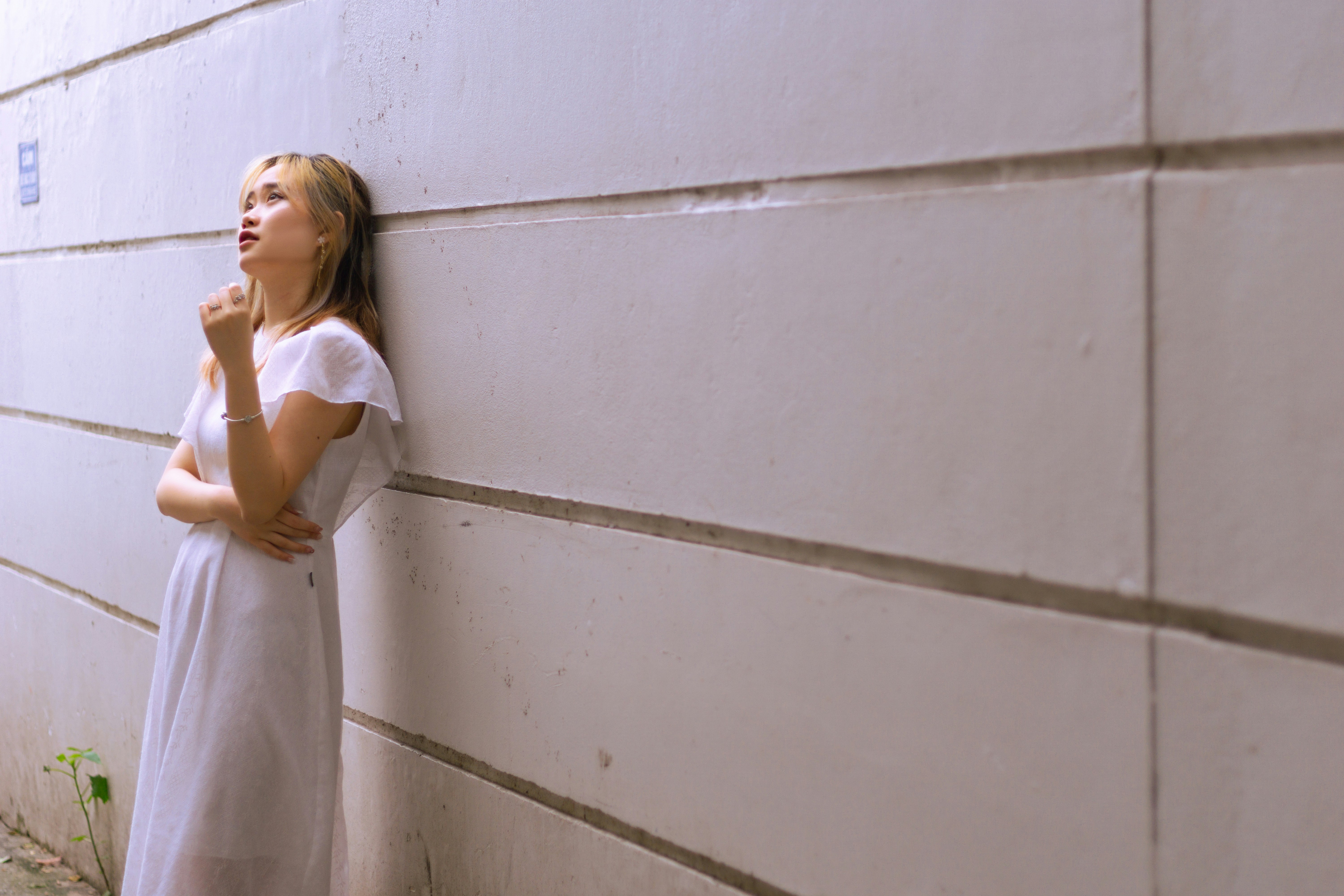 A woman leaning against a wall with her hand on her chin photo – Free ...