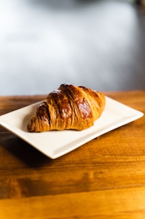 a croissant sitting on a white plate on a wooden table