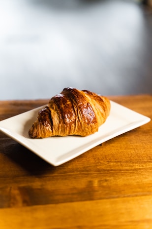 a croissant sitting on a white plate on a wooden table