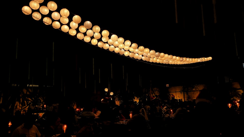 a group of people sitting around a table with paper lanterns hanging from the ceiling