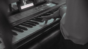 A musician adjusting chords on a keyboard while following lyrics on a tablet screen.