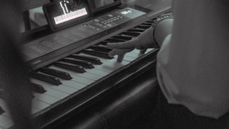 A musician adjusting chords on a keyboard while following lyrics on a tablet screen.