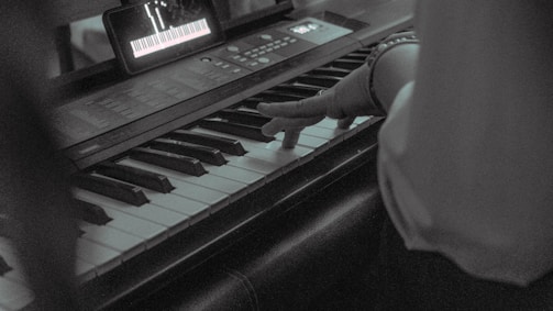 A smiling older adult playing piano with sheet music and a tablet nearby.
