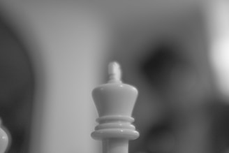 A black and white image featuring a close-up of a chess piece, specifically a white king, against a blurred background.