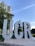 Large, metallic letters 'UCR' are prominently displayed in an outdoor setting. Behind the letters, there is a tall tower structure visible through the foliage of the surrounding trees. The sky is clear with a few wispy clouds, suggesting fair weather.
