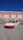 A modified white sports car with a red front bumper is parked on a street in front of a building with a blue sky in the background. The car has lowered suspension and custom wheels.