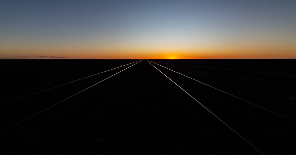 Una vía de tren con la puesta de sol en el fondo