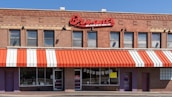 A brick building houses a barbecue restaurant with a red and white striped awning. Large red signage displays the name 'Bryant's Barbeque' above the windows. There are multiple windows with a few signs and posters visible. The main entrance is flanked by additional doors and brick walls.