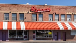 A brick building houses a barbecue restaurant with a red and white striped awning. Large red signage displays the name 'Bryant's Barbeque' above the windows. There are multiple windows with a few signs and posters visible. The main entrance is flanked by additional doors and brick walls.