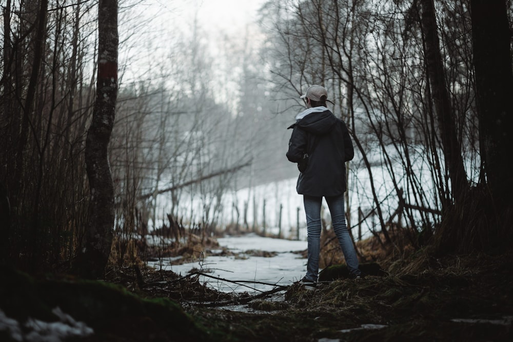 uma pessoa de pé na floresta olhando para a neve