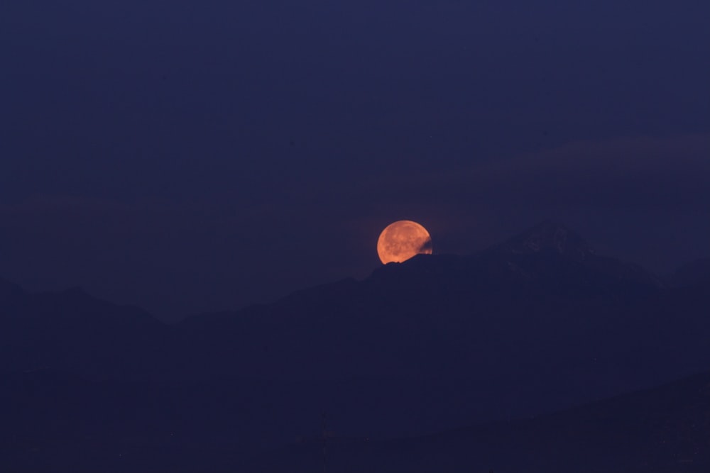 a full moon rising over a mountain range