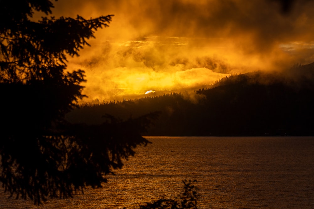 the sun is setting over a lake with trees in the foreground