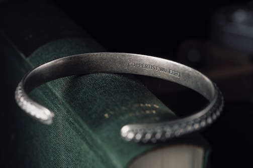 A silver bracelet with intricate details wrapped gently around a vintage book.