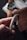 A hand holding a detailed, intricately designed metallic bracelet with a central gold accent. In the background, a blurred watch with a leather strap and part of a wooden item are visible.