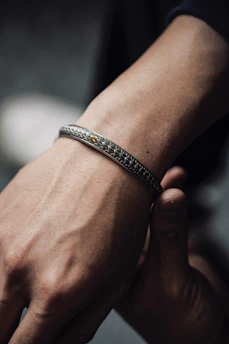 Close-up of a sleek black and gold bangle resting on ivory silk fabric under soft lighting.