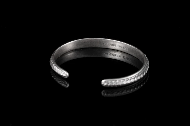 Close-up of a sleek, industrial-style bracelet with a subtle engraved message.