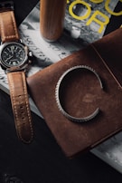 A stylish wristwatch with a leather strap resting on a stack of fashion magazines.