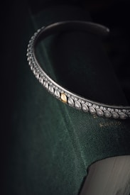 A metallic accessory with intricate leaf patterns and a single gold accent is resting on a dark green book. The detailed artwork on the metal creates a vintage and elegant appearance.