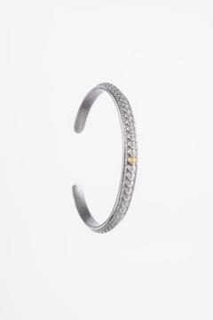 A silver bracelet with intricate decorative patterns along its exterior. The bracelet has an open-ended design and a small bronze or golden accent near the opening.