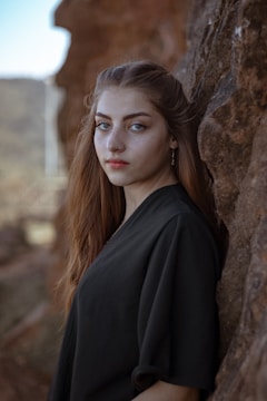 a woman with long hair leaning against a rock
