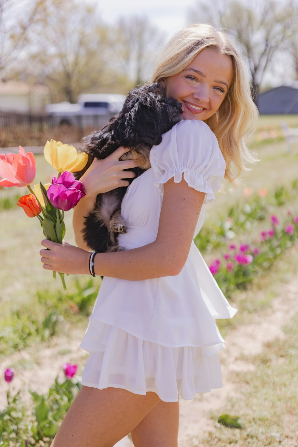 a woman in a white dress holding a dog and flowers
