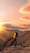 A joyful traveler standing on a lush Ecuadorian mountain trail with a vibrant sunset behind a volcano silhouette.