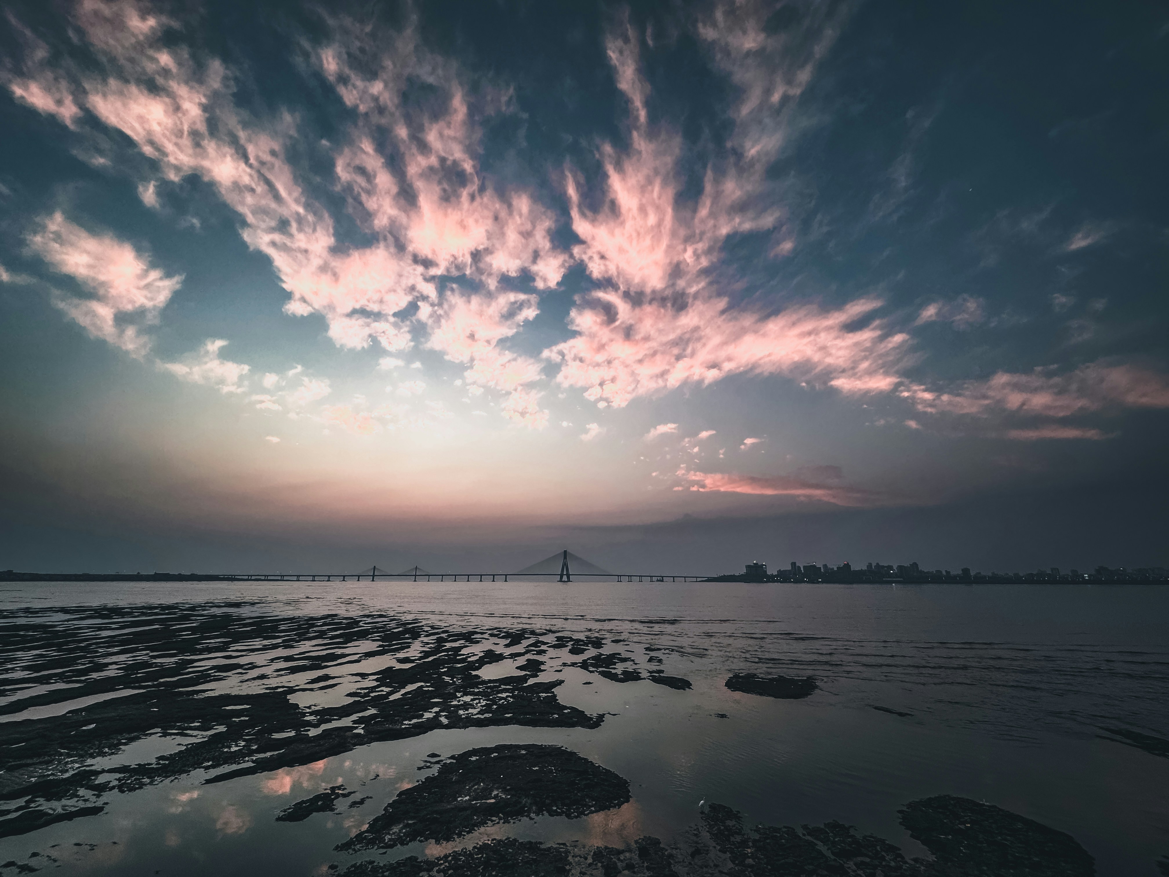 a sunset over a body of water with a bridge in the distance