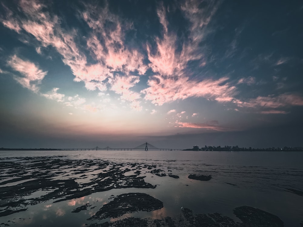 a sunset over a body of water with a bridge in the distance