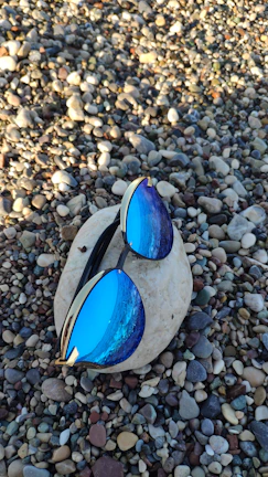 A pair of modern sunglasses with subtle gold accents placed on a black obsidian stone.