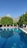 A tranquil outdoor swimming pool surrounded by sun loungers and white umbrellas, set against a backdrop of lush green trees and majestic mountains in the distance.