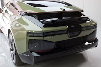 A sleek, modern car with a glossy finish, showcasing an aerodynamic design. The rear view highlights its broad tail lights, reflector features, and a prominent spoiler. Smooth lines and curves add to the futuristic appeal, with the car's mint green color contrasting the black accents.