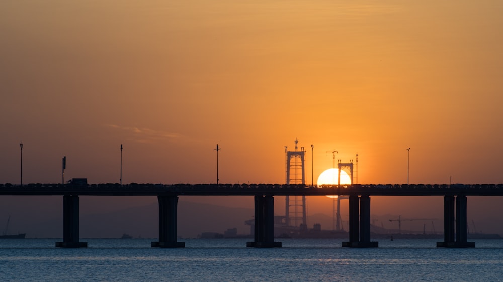 the sun is setting over a bridge over the water