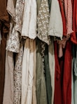 A collection of various dresses is lined up, showcasing a range of patterns and fabrics. The dresses include floral prints, gingham patterns, and solid colors, hung closely together.