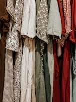 A collection of various dresses is lined up, showcasing a range of patterns and fabrics. The dresses include floral prints, gingham patterns, and solid colors, hung closely together.