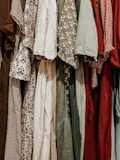 A collection of various dresses is lined up, showcasing a range of patterns and fabrics. The dresses include floral prints, gingham patterns, and solid colors, hung closely together.
