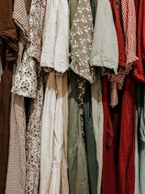 A collection of various dresses is lined up, showcasing a range of patterns and fabrics. The dresses include floral prints, gingham patterns, and solid colors, hung closely together.