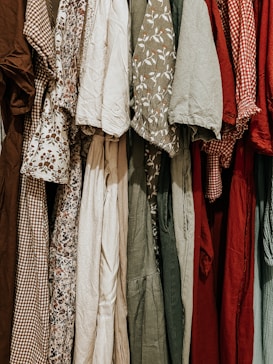 A collection of various dresses is lined up, showcasing a range of patterns and fabrics. The dresses include floral prints, gingham patterns, and solid colors, hung closely together.
