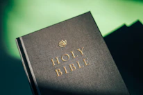 Elegant close-up of an open Bible with a golden cross bookmark resting on deep green fabric.