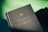 A close-up view of a hardcover book with the title 'Holy Bible' embossed in gold lettering on a textured black cover. The book is angled slightly with a soft green background.