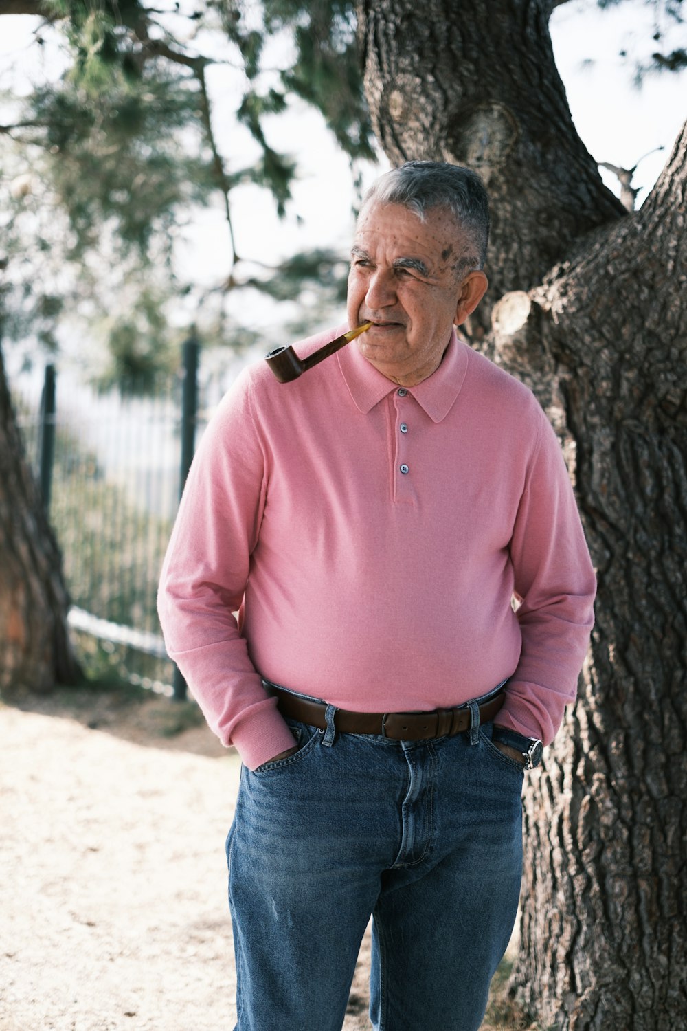 a man standing next to a tree with a pipe in his mouth