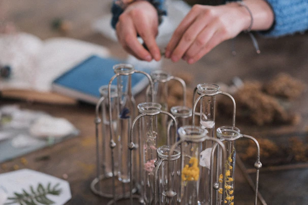 Softly lit close-up of a researcher’s hands carefully handling delicate glassware filled with vibrant botanical extracts.