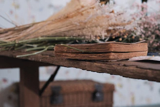 Close-up of a book surrounded by leaves and small wildflowers on a rustic wooden table.
